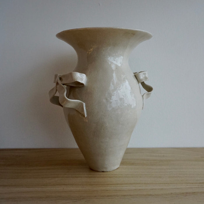 Beige ceramic vase with handles on a wooden surface and white background.  Amelia Christoffers | Shop Fodder