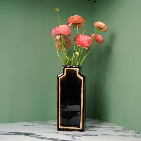 deep glossy black vase with pink flowers on a green background. 