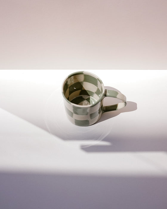 Green ceramic mug on a reflective surface with a gradient background. Fern Taylor Nerikomi Ceramics. Fodder