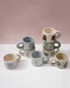 Set of ceramic mugs with various designs on a white surface and pink background. Portrait Mug | Brutes London | Handmade Ceramics | Fodder