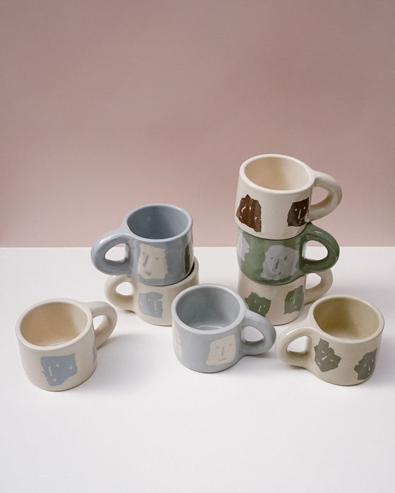 Set of ceramic mugs with various designs on a white surface and pink background. Portrait Mug | Brutes London | Handmade Ceramics | Fodder