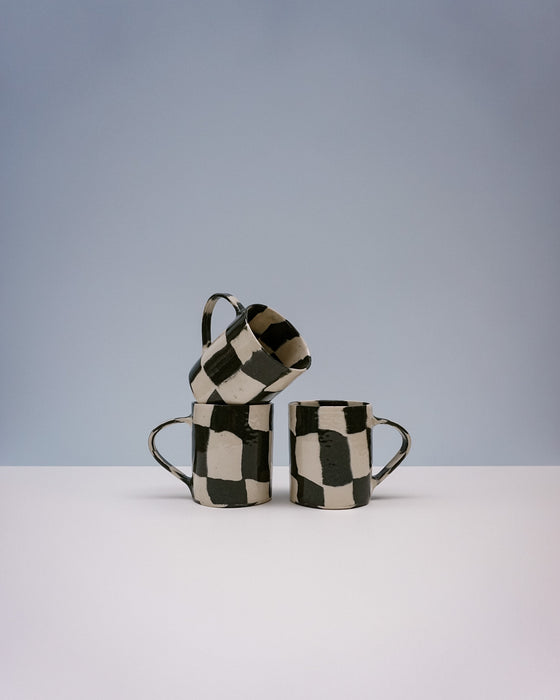 Three ceramic mugs with black and white checkered pattern on a light grey background. Checkerboard Nerikomi Ceramic Mug | Fern Taylor | Kentish Town Stores