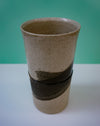 Ceramic vase with black band on a white surface against a green background. Janne Meijer Ceramics | Shop Fodder