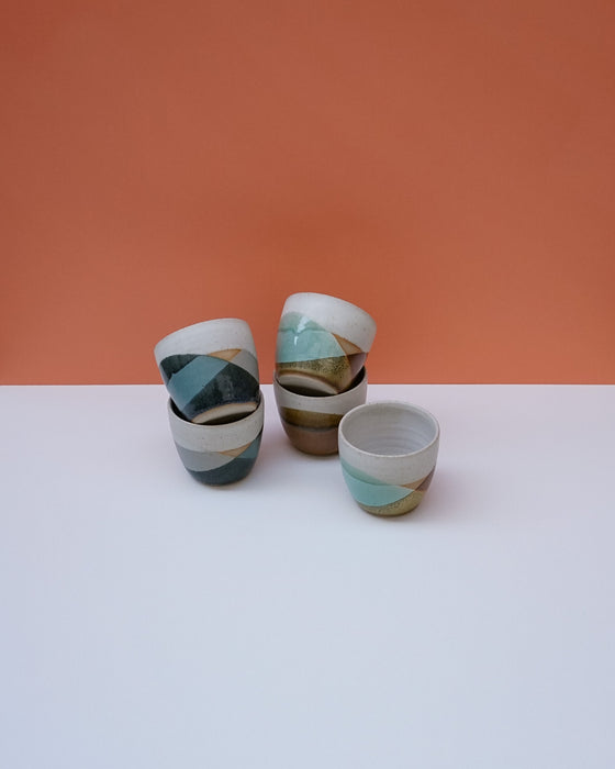 Set of ceramic cups with striped patterns on a white surface and orange background. Liz Vidal Ceramics | Shop Fodder