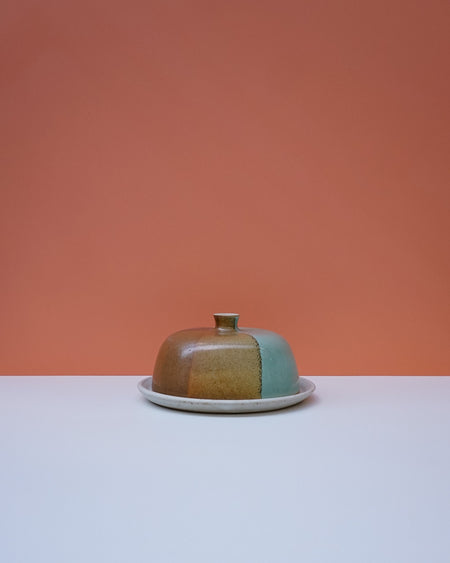 Ceramic butter dish with a lid on a white surface against an orange background. Liz Vidal Ceramics | Shop Fodder