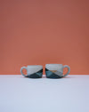 Two ceramic mugs with geometric design on a white surface and orange background. Liz Vidal Ceramics | Shop Fodder