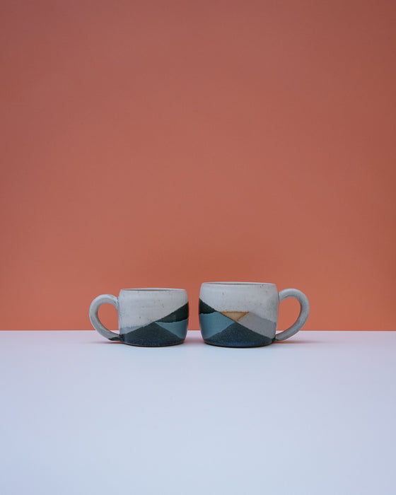Two ceramic mugs with geometric design on a white surface and orange background. Liz Vidal Ceramics | Shop Fodder