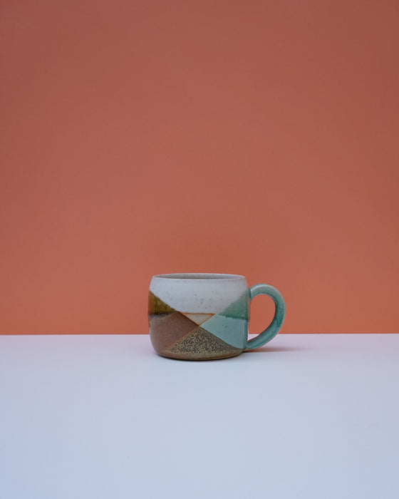 Ceramic mug with geometric design on a white surface and orange background. Liz Vidal Ceramics | Shop Fodder