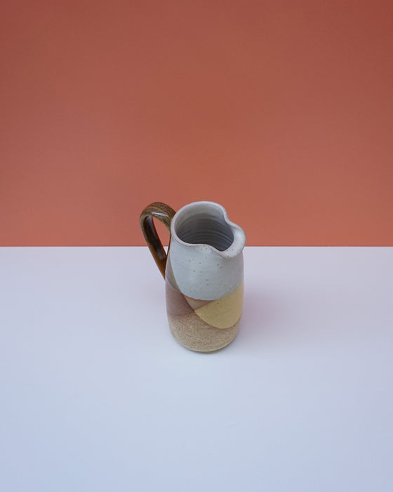 Ceramic pitcher with a gradient design on a white surface and orange background. Liz Vidal Ceramics | Shop Fodder
