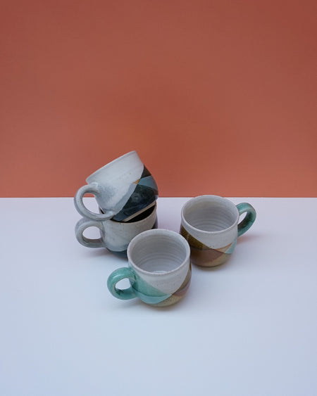 Three ceramic cups with green handles on a white surface against an orange background. Liz Vidal Ceramics | Shop Fodder
