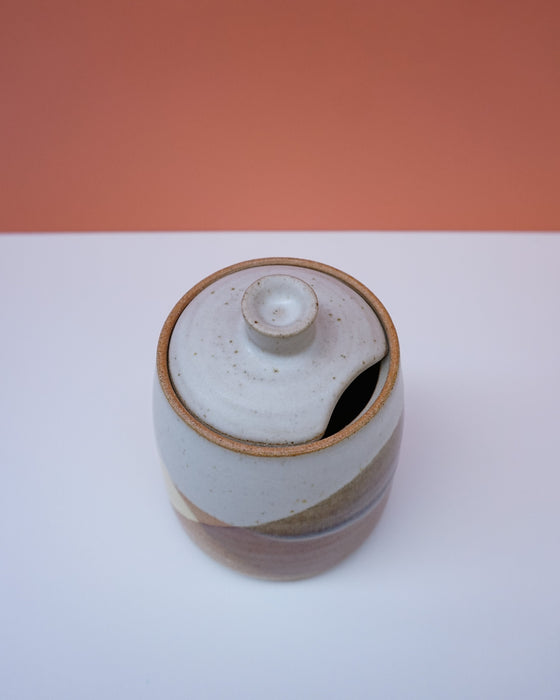 Ceramic jar with a lid on a white surface with an orange background. Liz Vidal Ceramics | Shop Fodder