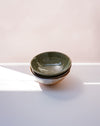 Three nested ceramic bowls with a speckled sage green glaze and a rustic brown rim, set on a white surface with soft natural light. Dinner Bowl | Scree Ceramics | Fodder