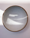 A top-down view of a handmade ceramic bowl with a speckled off-white interior and a rustic brown rim, set against a light background with soft shadows. Toasted Clay Dinner Bowl | Scree Ceramics | Fodder