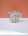 Ceramic pitcher with grid pattern on a white surface and peach background. Sophie Alda | Handmade Ceramics | Shop Fodder