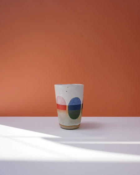 Ceramic cup with colorful design on a white surface and orange background. Sophie Alda | Handmade Ceramics | Shop Fodder