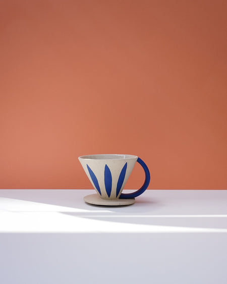 Ceramic coffee dripper with blue leaf designs on a white surface against an orange wall. Sophie Alda | Handmade Ceramics | Shop Fodder