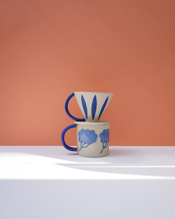 Ceramic mug with blue floral design and a matching funnel on a peach background. Sophie Alda | Handmade Ceramics | Shop Fodder