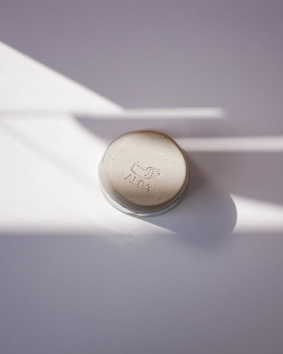 Round beige object with a brand logo on a light purple background. Sophie Alda | Handmade Ceramics | Shop Fodder