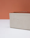 Close-up of the side of a rectangular ceramic box or planter in a matte warm off-white glaze, with a terracotta-colored top surface and a terracotta background. Studio ERS | Soup Vase | Fodder