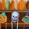 Halloween-themed masks and pumpkins on a fireplace mantle. East End Press | Shop Fodder