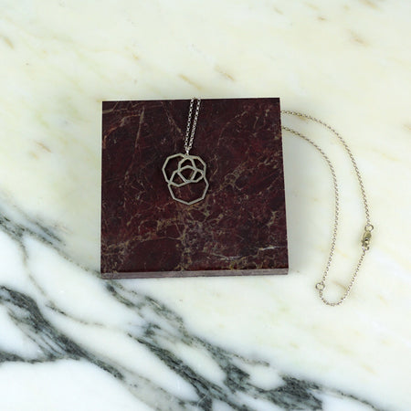 Necklace with a floral pendant on a maroon card against a marble background | Square_Dissarray_Pendant_Scarlett_Cohen_French_Shop_Fodder_