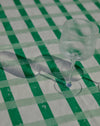 A clear ribbed glass wine glass on a green and white checkered tablecloth, casting a long shadow.