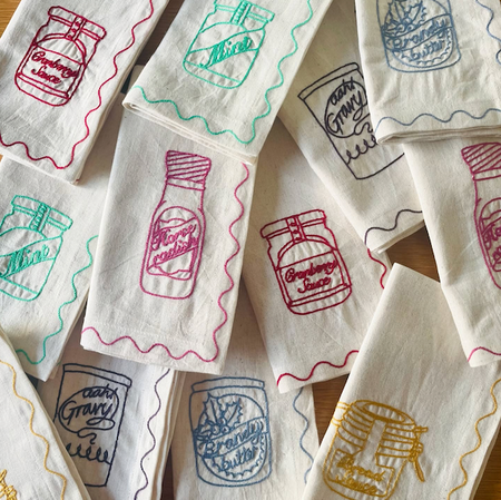 Set of embroidered towels with Gravy Boat designs on a wooden surface. See&Quin_Christmas_Phrases_Napkins_Shop_Fodder_2