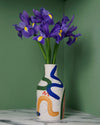 porcelain vase with abstract brushwork pattern and a bunch of iris flowers on a green background. 
