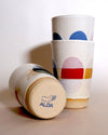 three cups with multi coloured dots painted around the side. one is lying down to show the makers mark of Sophie Alda. 