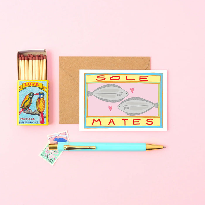 a small card with two fishes and a message that reads Sole mates spelt S O L E. next to a match box and a pen. 